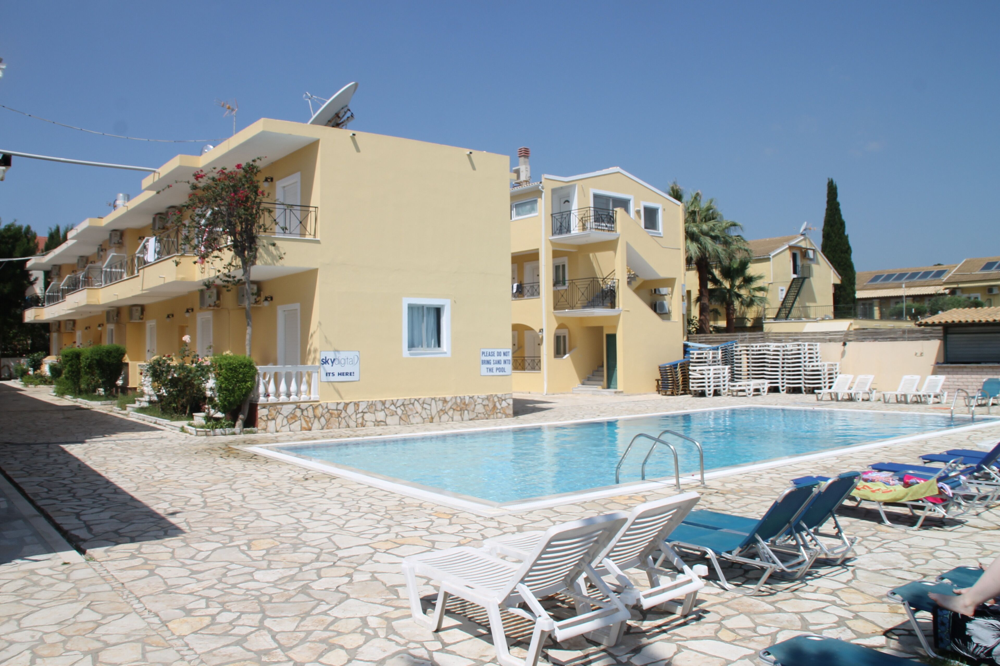 A pool area with lounge chairs, a clear blue pool, and a building with balconies and a sign that reads "Please do not touch the pool."