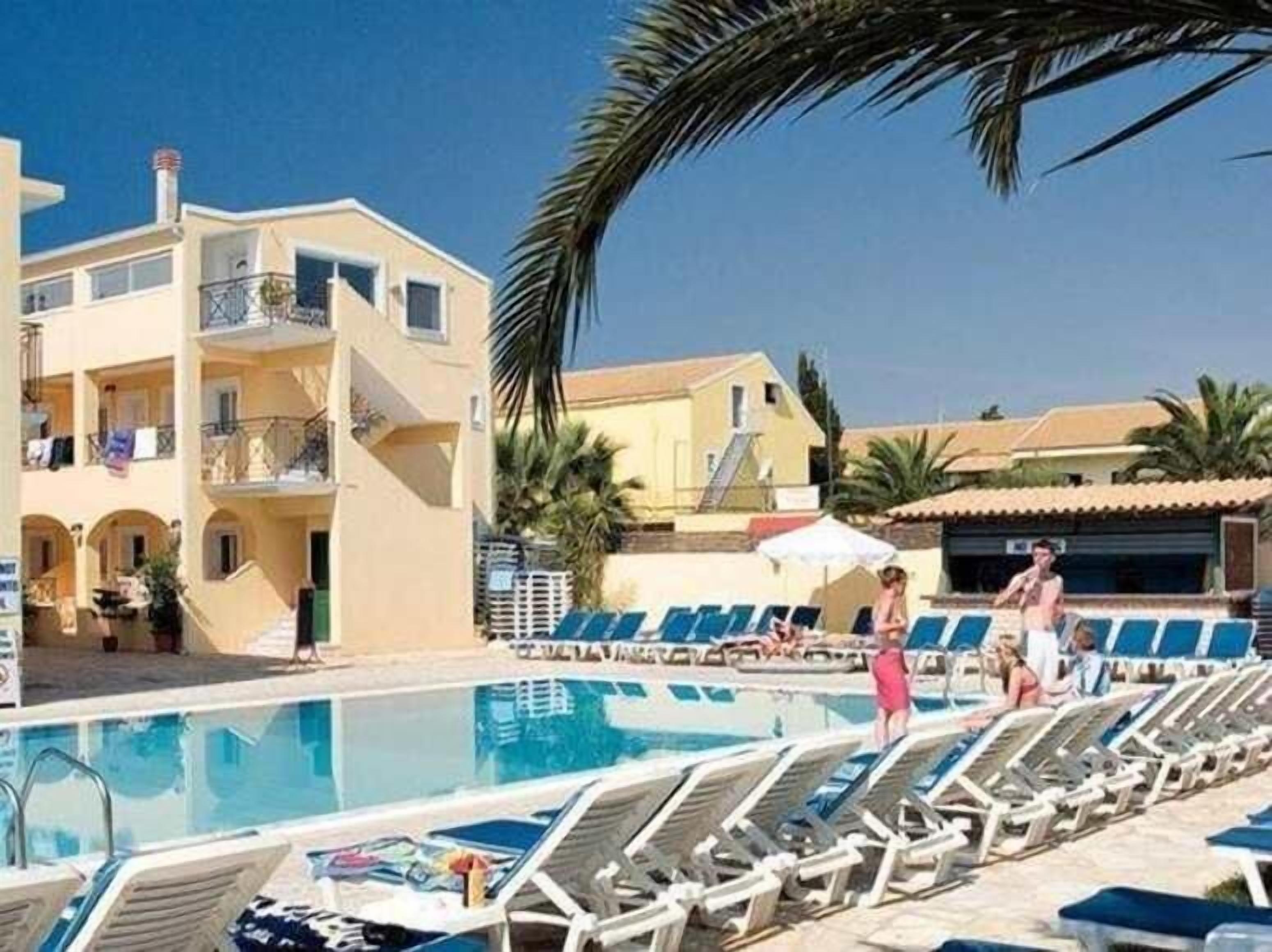 A poolside area with lounge chairs, a pool, and a building with balconies.
