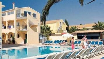 A poolside area with lounge chairs, a pool, and a building with balconies.