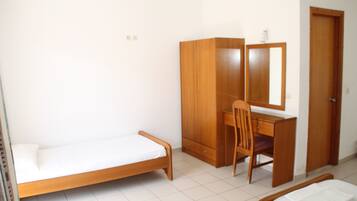 A small, clean room with a single bed, a wooden desk with a chair, a wardrobe, and a door.