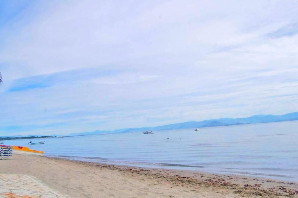 Una playa con agua tranquila, barcos y montañas a lo lejos.