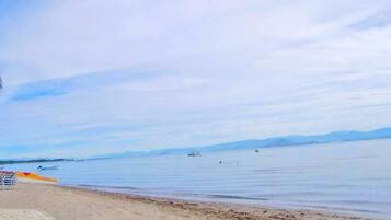Una playa con agua tranquila, barcos y montañas a lo lejos.