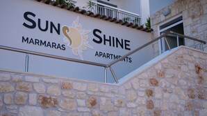 Un cartel para 'SUNSHINE MARMARAS APARTMENTS' con fachada de piedra y barandilla metálica.