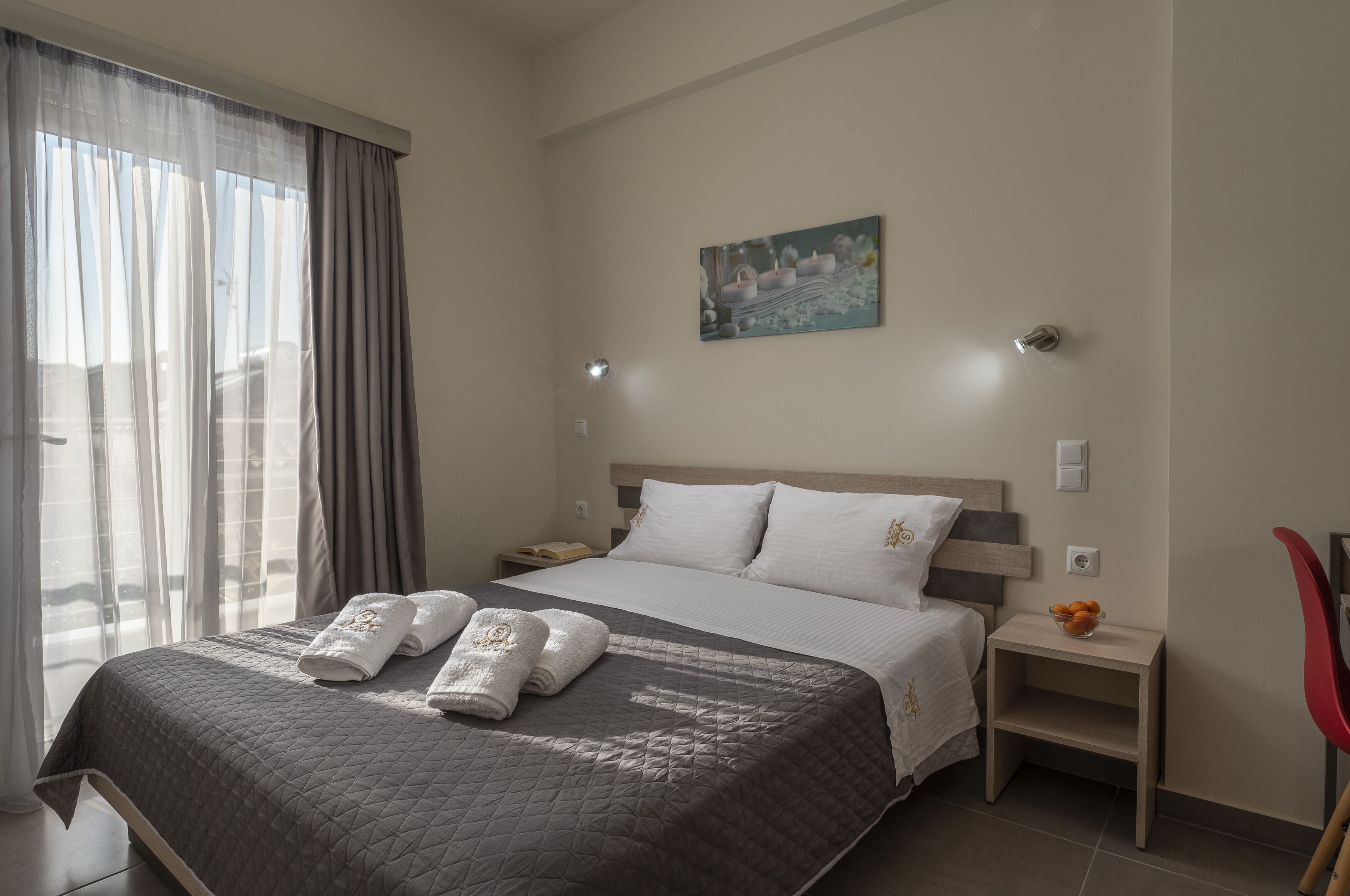 Una habitación de hotel con cama, mesita de noche, una silla roja y un cuadro en la pared.