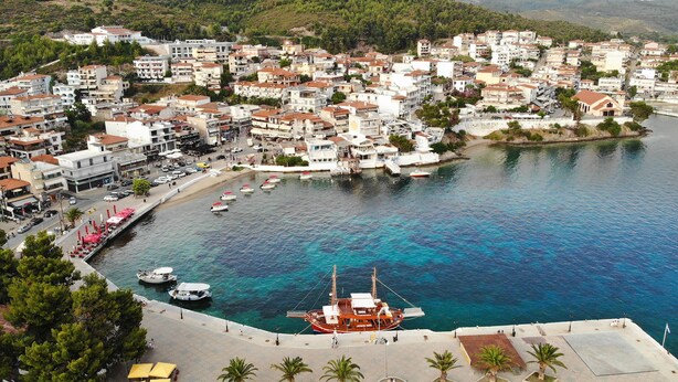 Un pueblo costero con un puerto deportivo, edificios con techos de tejas rojas y un mar azul cristalino.