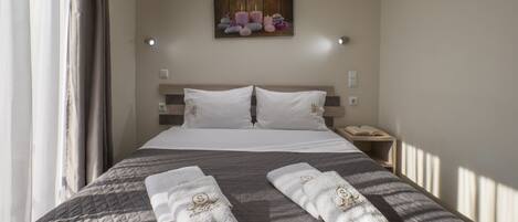 Habitación de hotel con una cama grande, dos almohadas, una mesita de noche con un libro y un cuadro en la pared.