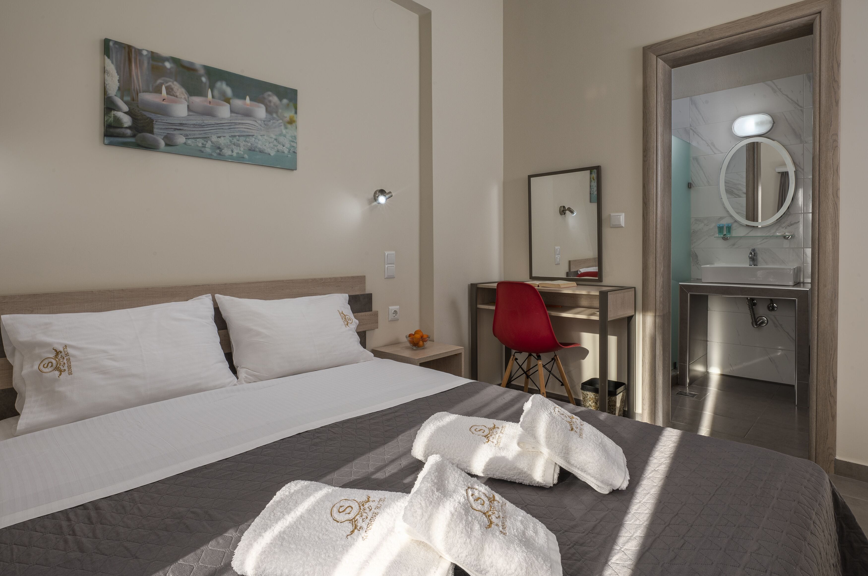 A hotel room with a bed, a desk, a red chair, a bathroom with a mirror and sink.