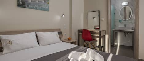 A hotel room with a bed, a desk, a red chair, a bathroom with a mirror and sink.