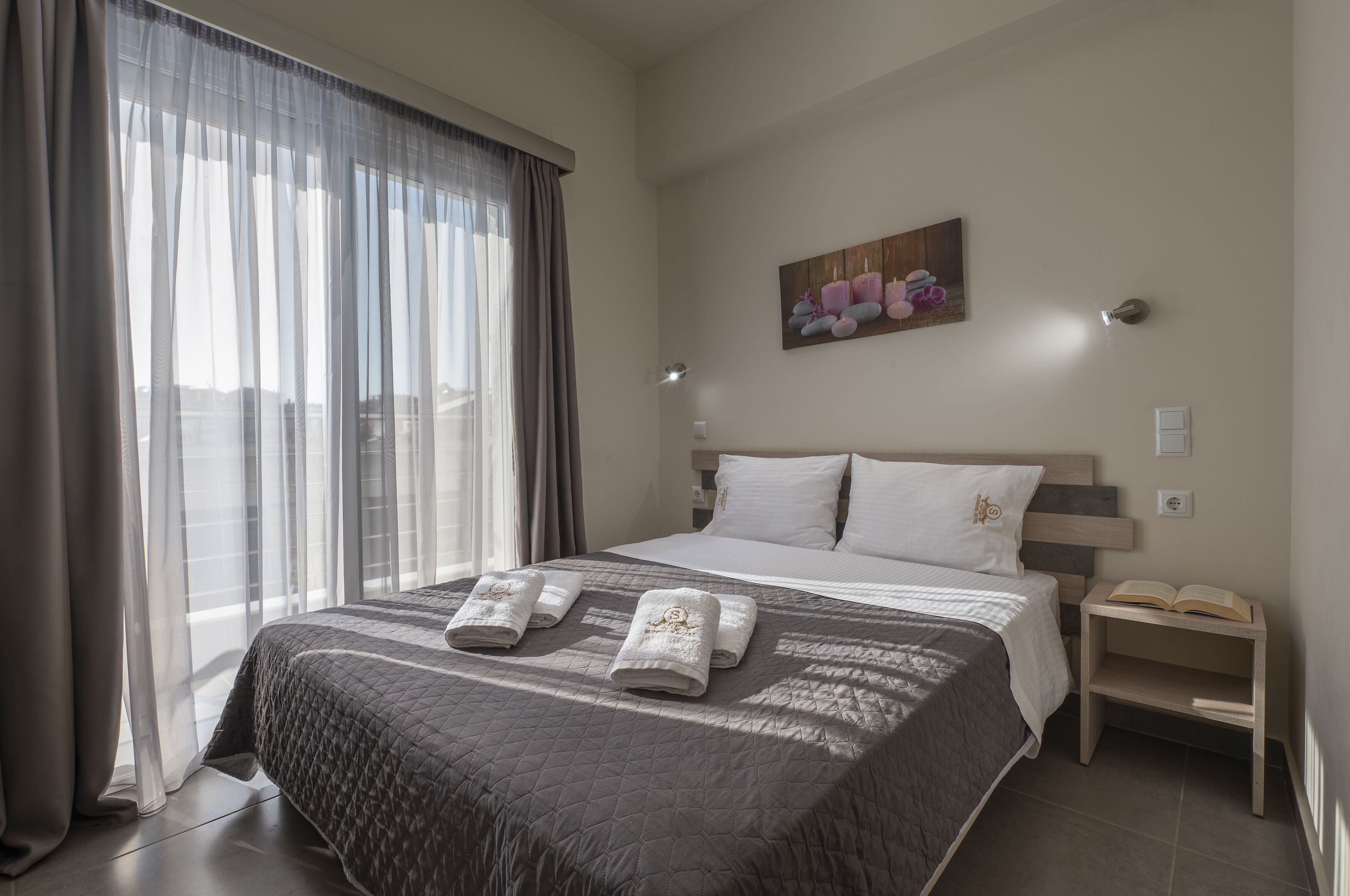 A modern hotel room with a large bed, a bedside table with a lamp, and a painting on the wall.