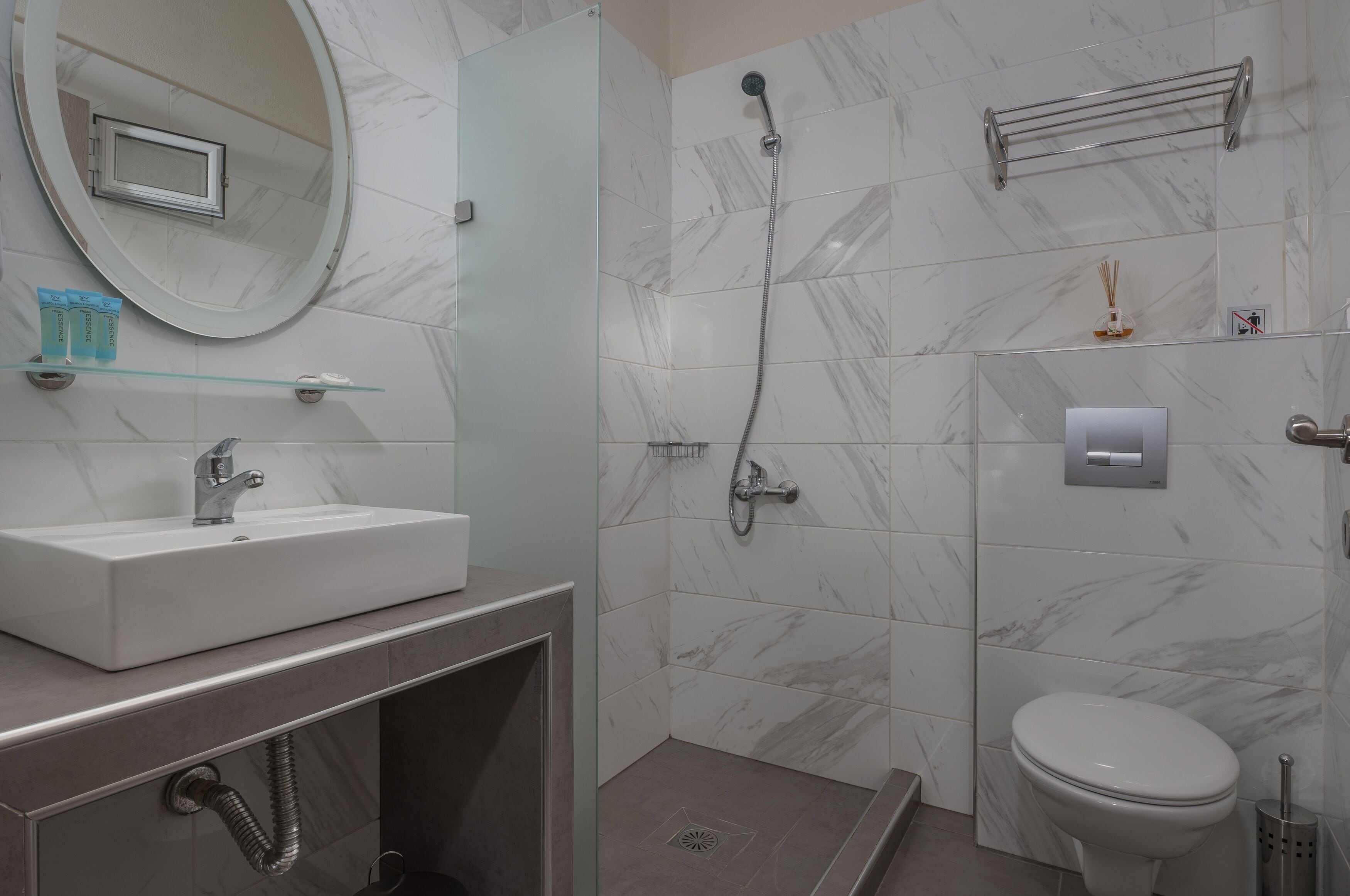 Ein modernes Badezimmer mit Dusche aus Marmorfliesen, einem Waschbecken mit Glasabdeckung und einer Toilette.