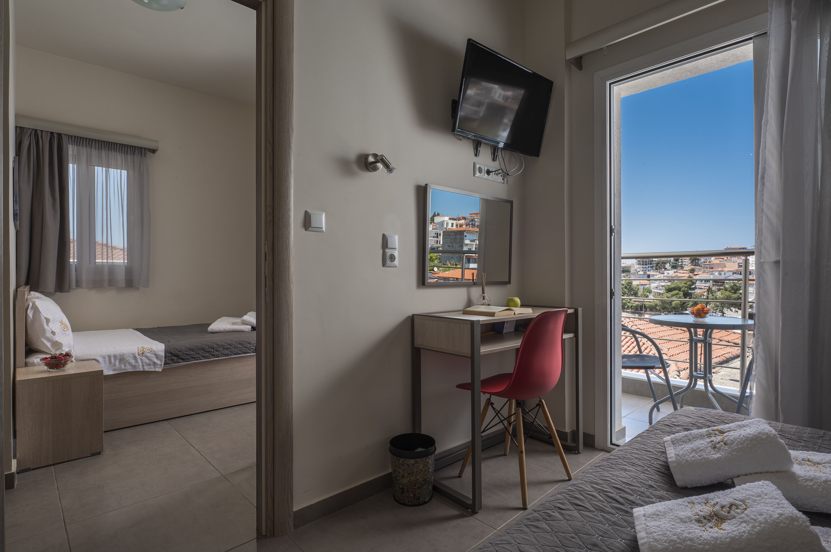 A hotel room with a bed, a desk, a chair, a TV, and a balcony with a view of the city.