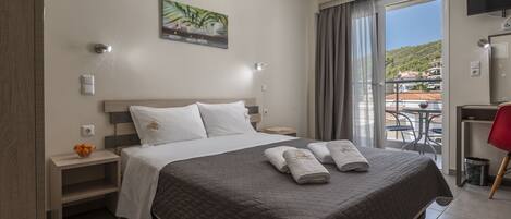 Ein Hotelzimmer mit einem großen Bett, einem Schreibtisch mit Stuhl, einem Fernseher und einem Balkon mit Blick auf die Stadt.