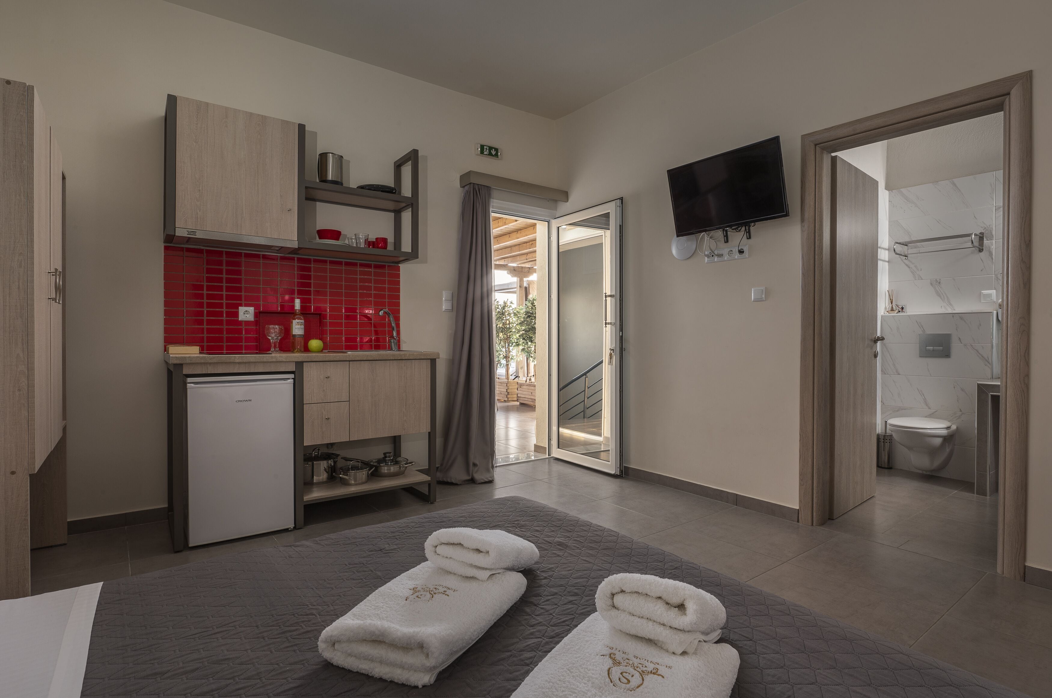 A modern hotel room with a kitchenette, a TV, and a bathroom.