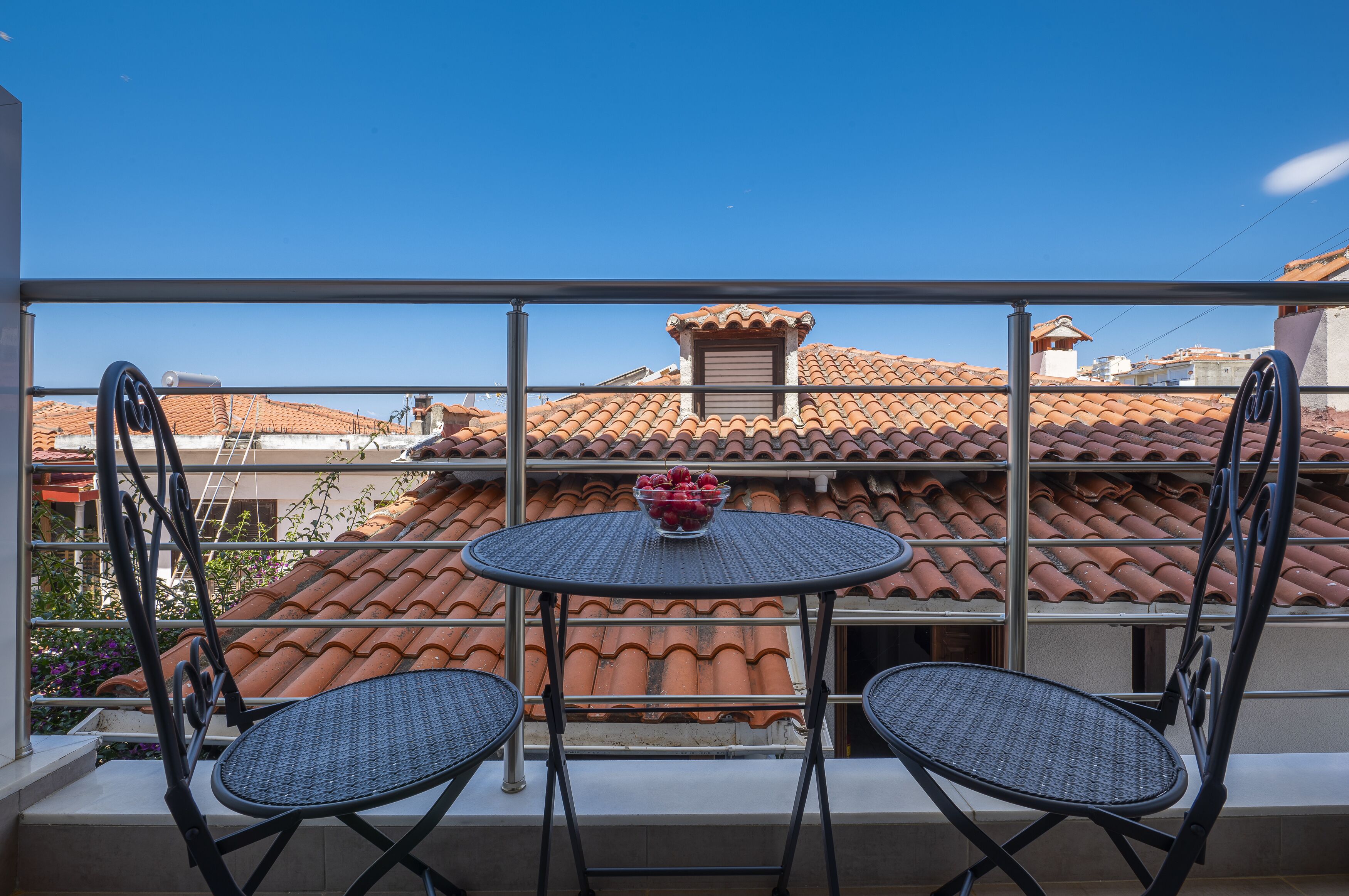 A balcony with two chairs and a table, overlooking a building with terracotta roof tiles.