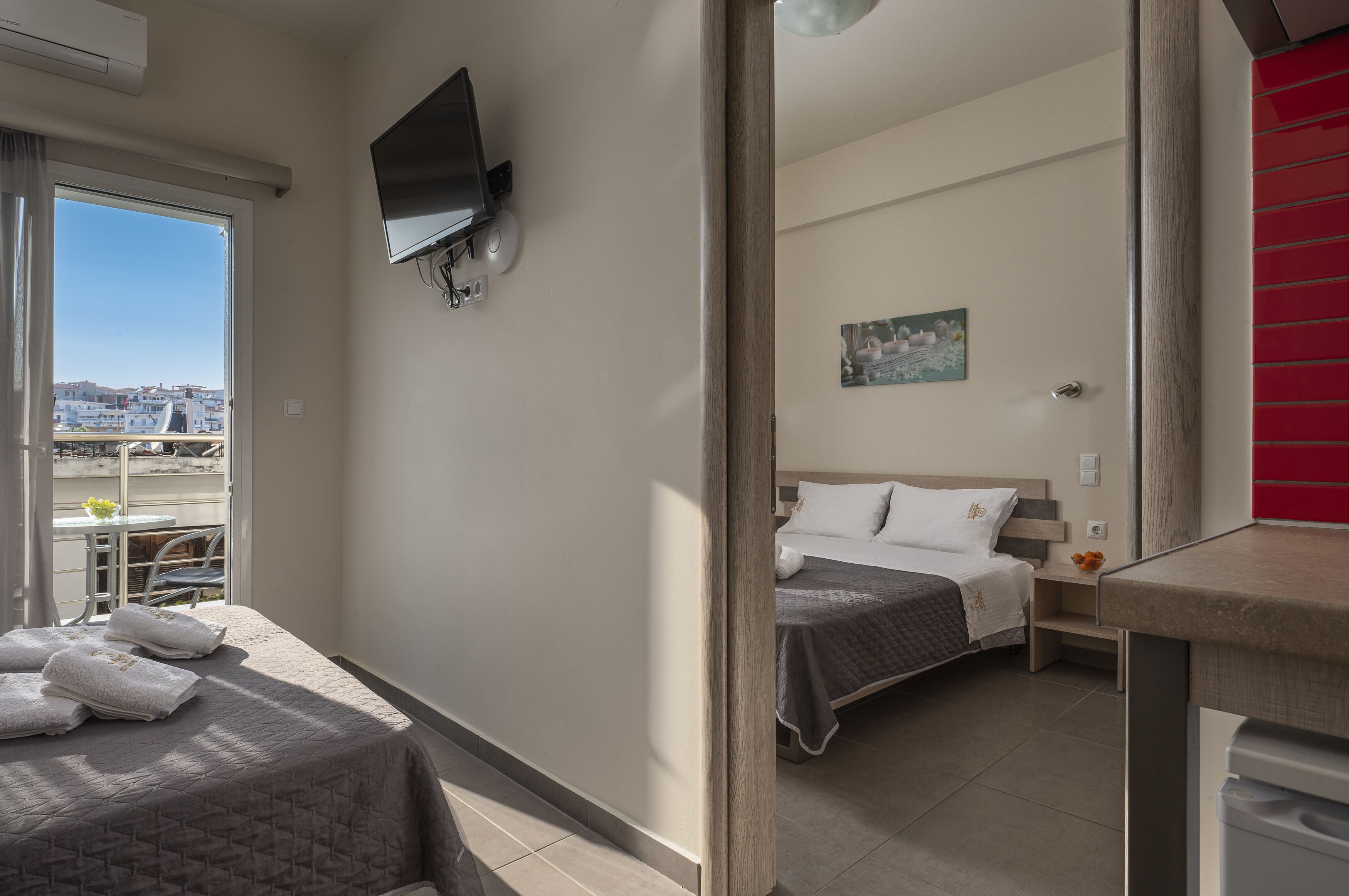 A hotel room with a bed, a TV, a balcony with a view of the city, and a red cabinet.