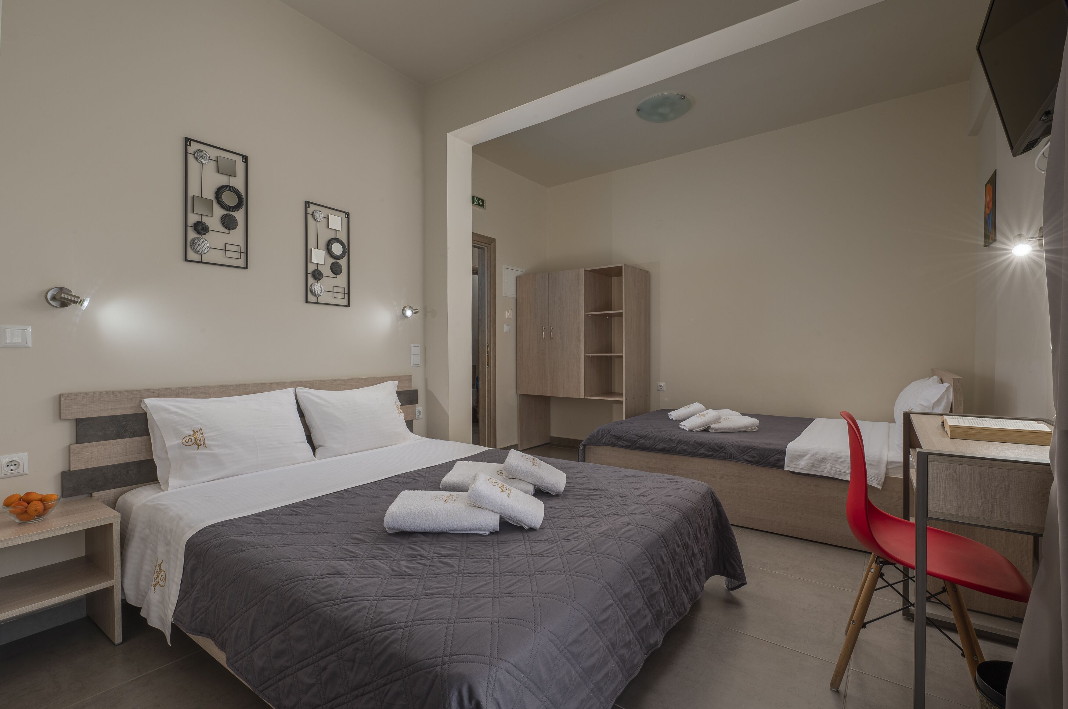 A hotel room with a large bed, a smaller bed, a desk, a chair, and a wardrobe.