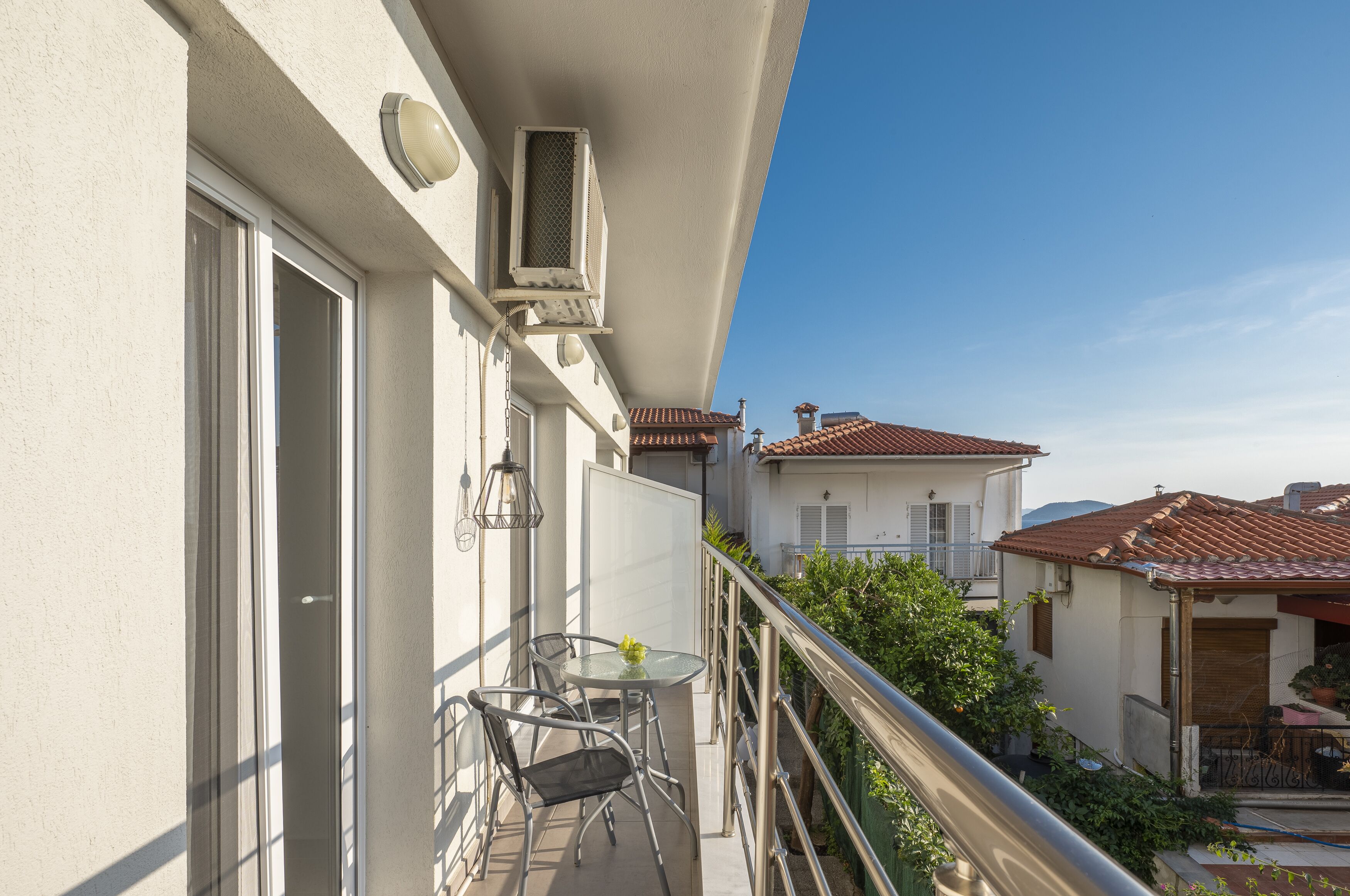A balcony with a glass table and chairs, a small potted plant, and a view of neighboring buildings.