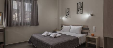 A neatly arranged bedroom with a bed, bedside tables, a nightstand, a wall-mounted light, and a window with curtains.