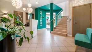 Un hall d’hôtel avec un mur d’accent de couleur turquoise, un escalier et un comptoir d’accueil.