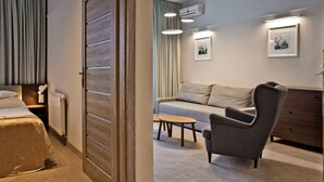 Une chambre d’hôtel moderne avec un lit, un canapé, une chaise et une petite table. Deux tableaux encadrés ornent le mur et un radiateur est posé sur le sol.