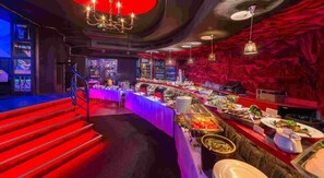 En buffet med et udvalg af mad, en trappe til et højere niveau og et barområde med røde og lilla farver.