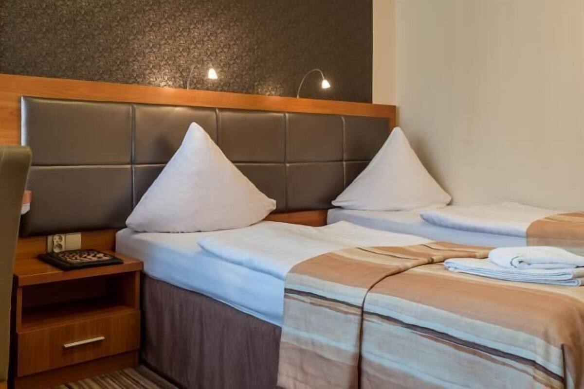 Een hotelkamer met twee bedden, een houten nachtkastje, een stoel en een kleine tafel met een telefoon en een boek.