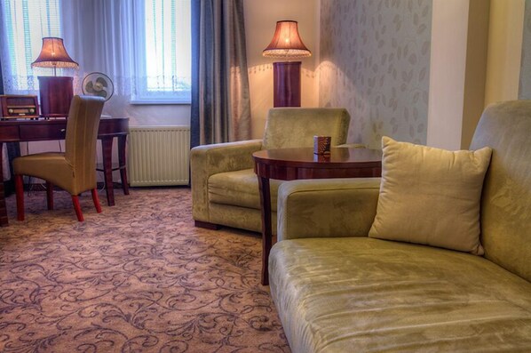 Un salón acogedor con un sofá, sillones, una mesita y un escritorio con una lámpara y un radio.