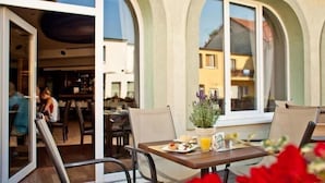 Un espace extérieur aménagé pour prendre les repas, avec une table dressée pour deux personnes, une plante en pot et une vue sur la rue.