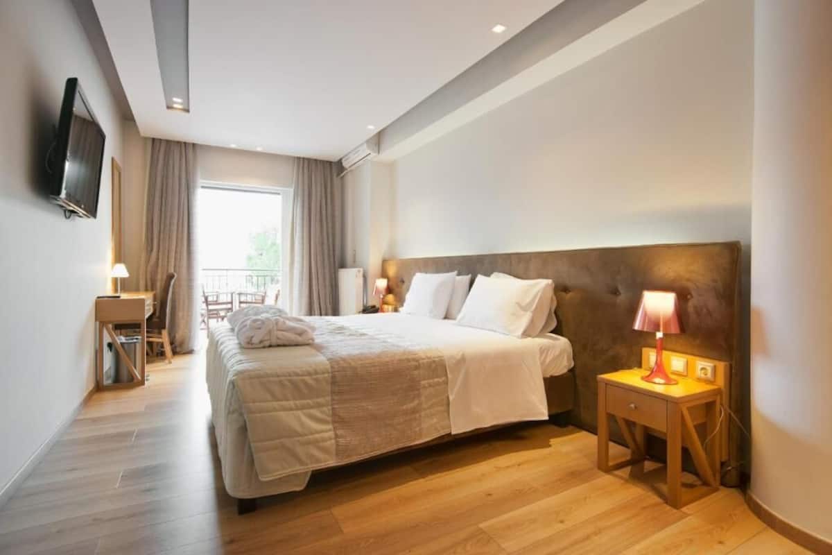 Habitación de hotel con una cama grande, mesitas de noche, un televisor montado en la pared y vistas al exterior.