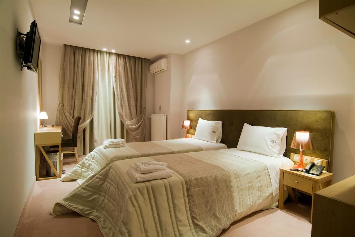 Habitación de hotel con dos camas, un escritorio, una silla, un televisor y una mesita de noche con lámpara y teléfono.