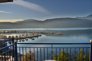 A lakeside view with a balcony railing, calm water, distant mountains, and a clear sky.