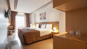A hotel room with a large bed, bedside tables, a desk, and a TV mounted on the wall. - Trokadero Hotel (Delphi)