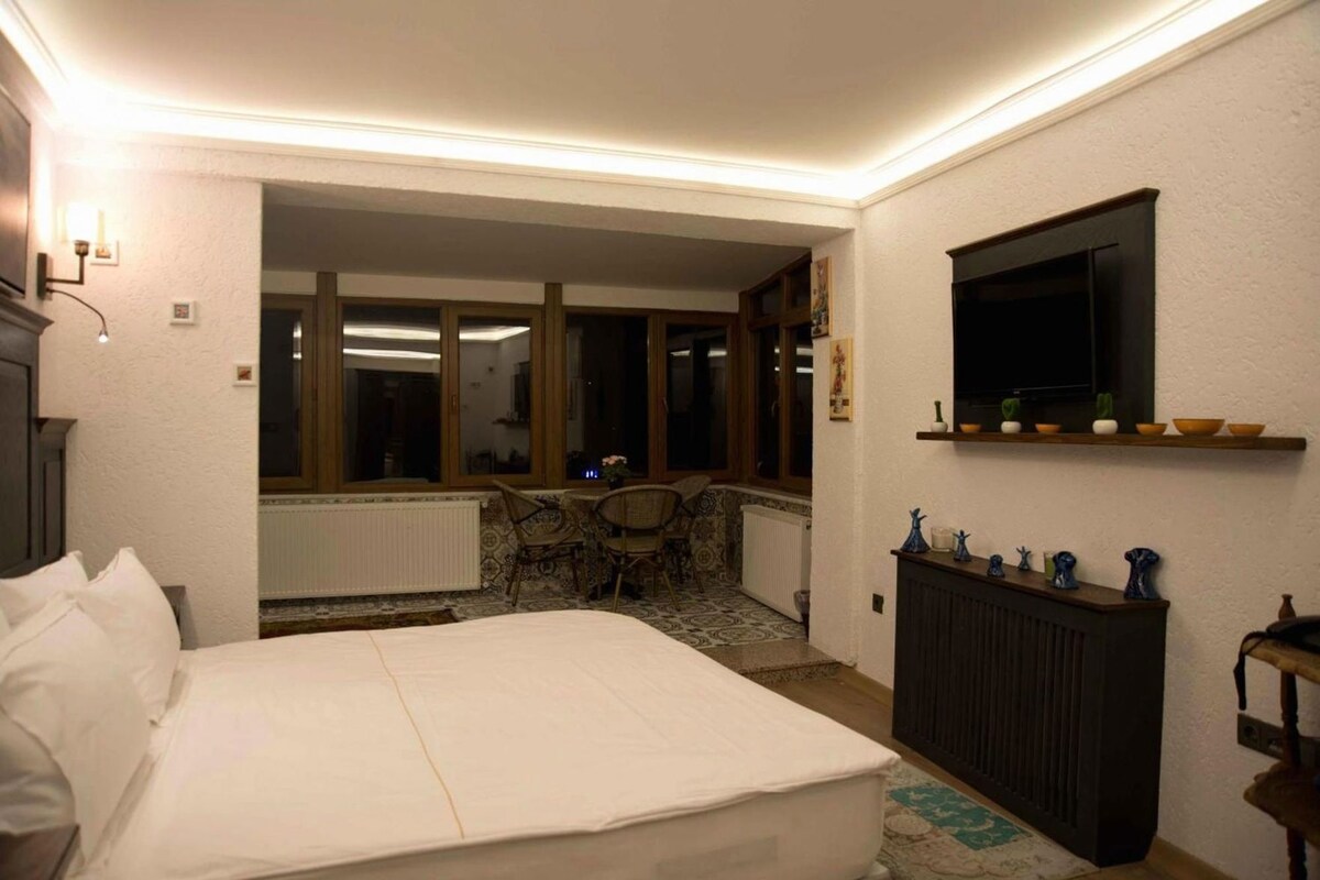 Un dormitorio con una cama, televisión montada en la pared, un radiador y una ventana.