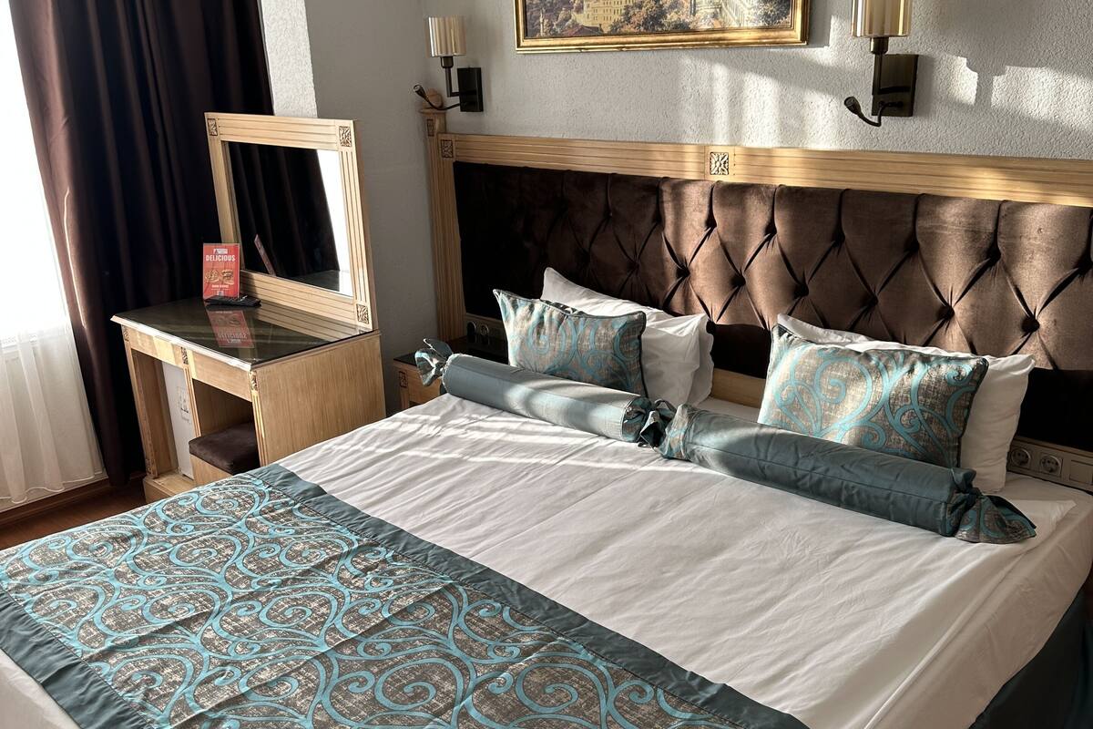 A neatly made bed with a patterned bedspread, a headboard with a tufted design, and a framed picture above the bed.