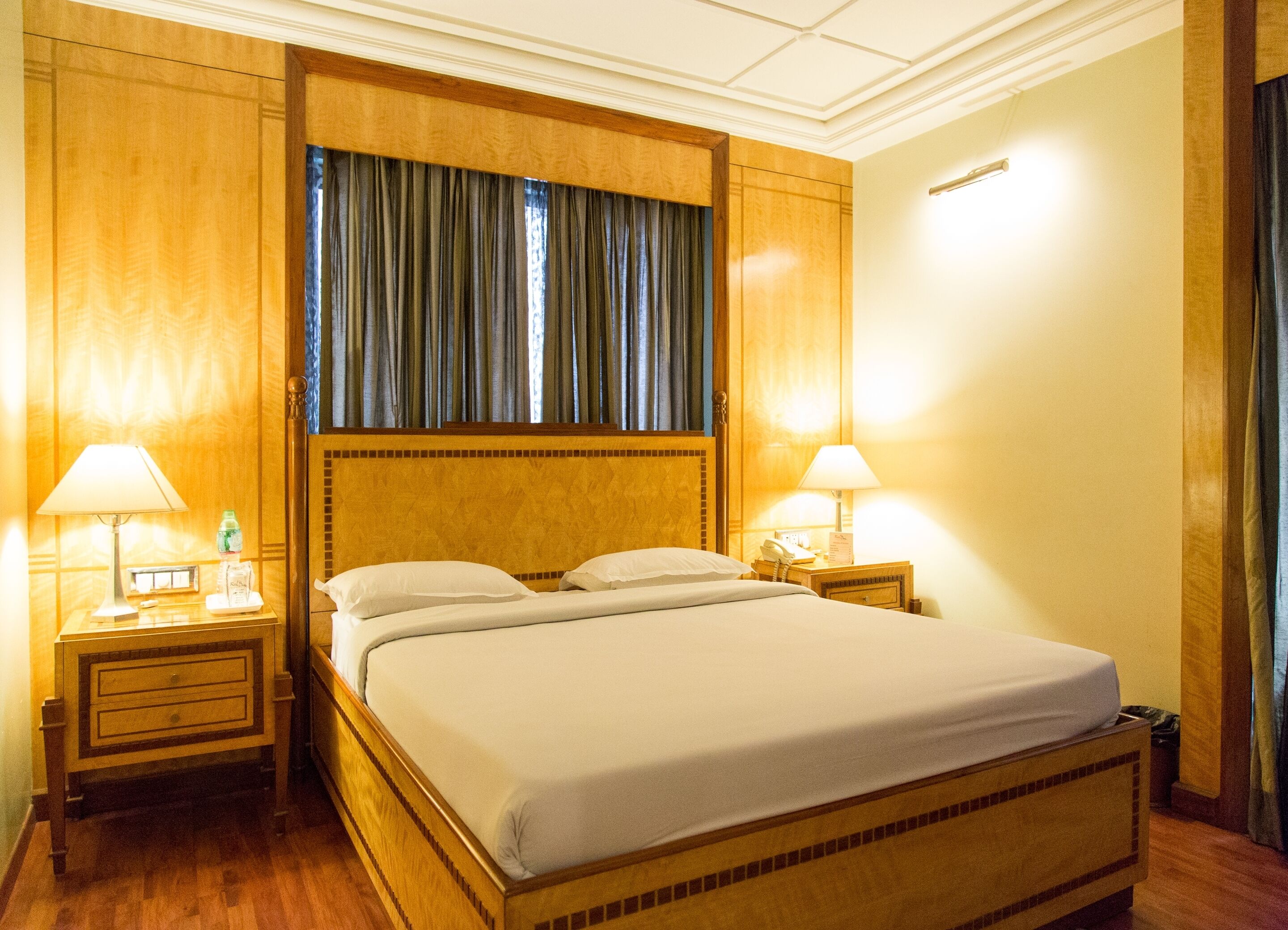 A hotel room with a large bed, two bedside tables, a nightstand, a lamp, and a window with curtains.