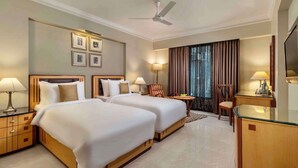 A hotel room with two beds, a desk, a chair, a TV, and a ceiling fan. - Sarovar Portico Kalupur Ahmedabad (Ahmedabad)
