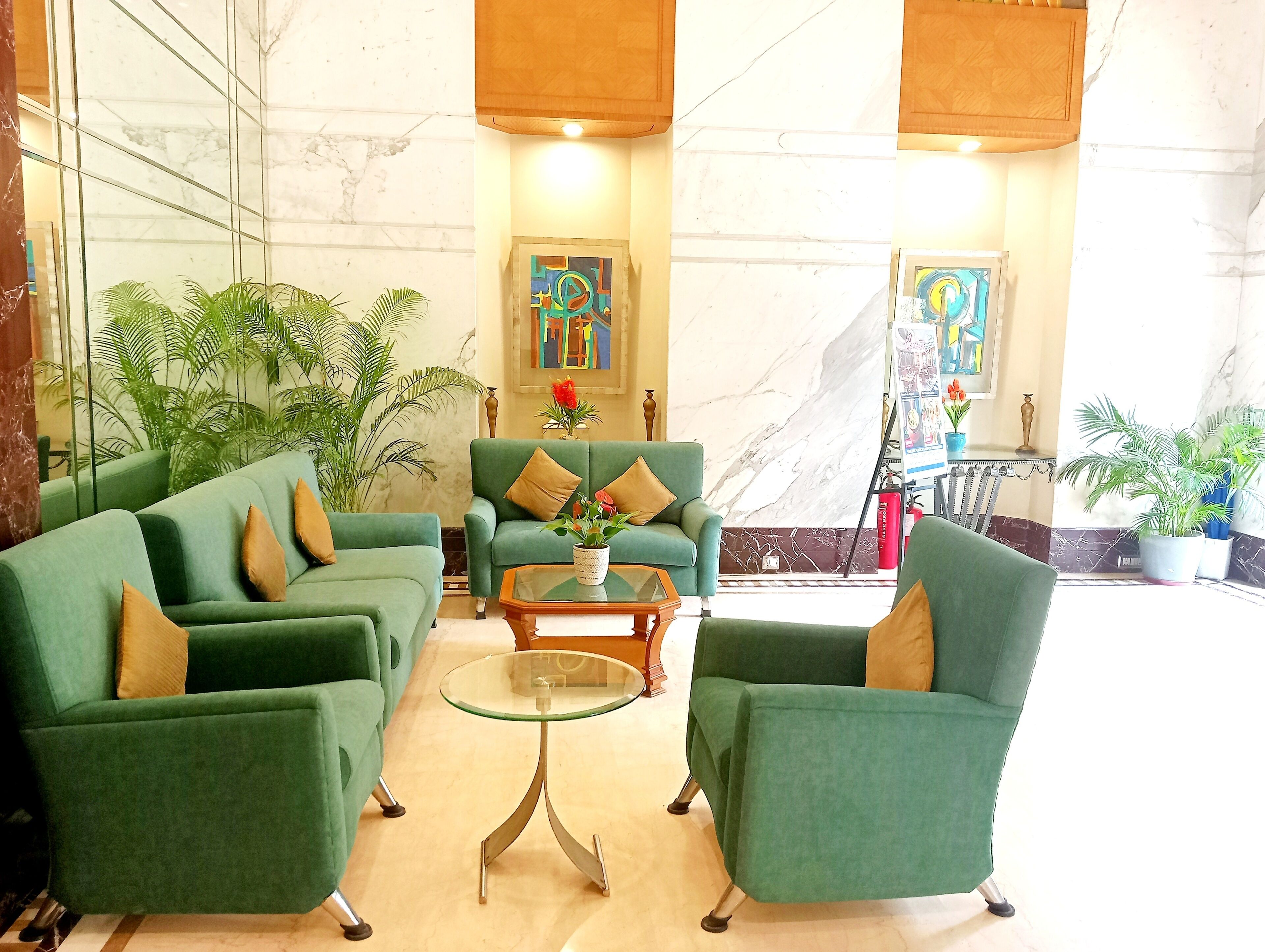 A lobby with green sofas, a glass coffee table, and potted plants.