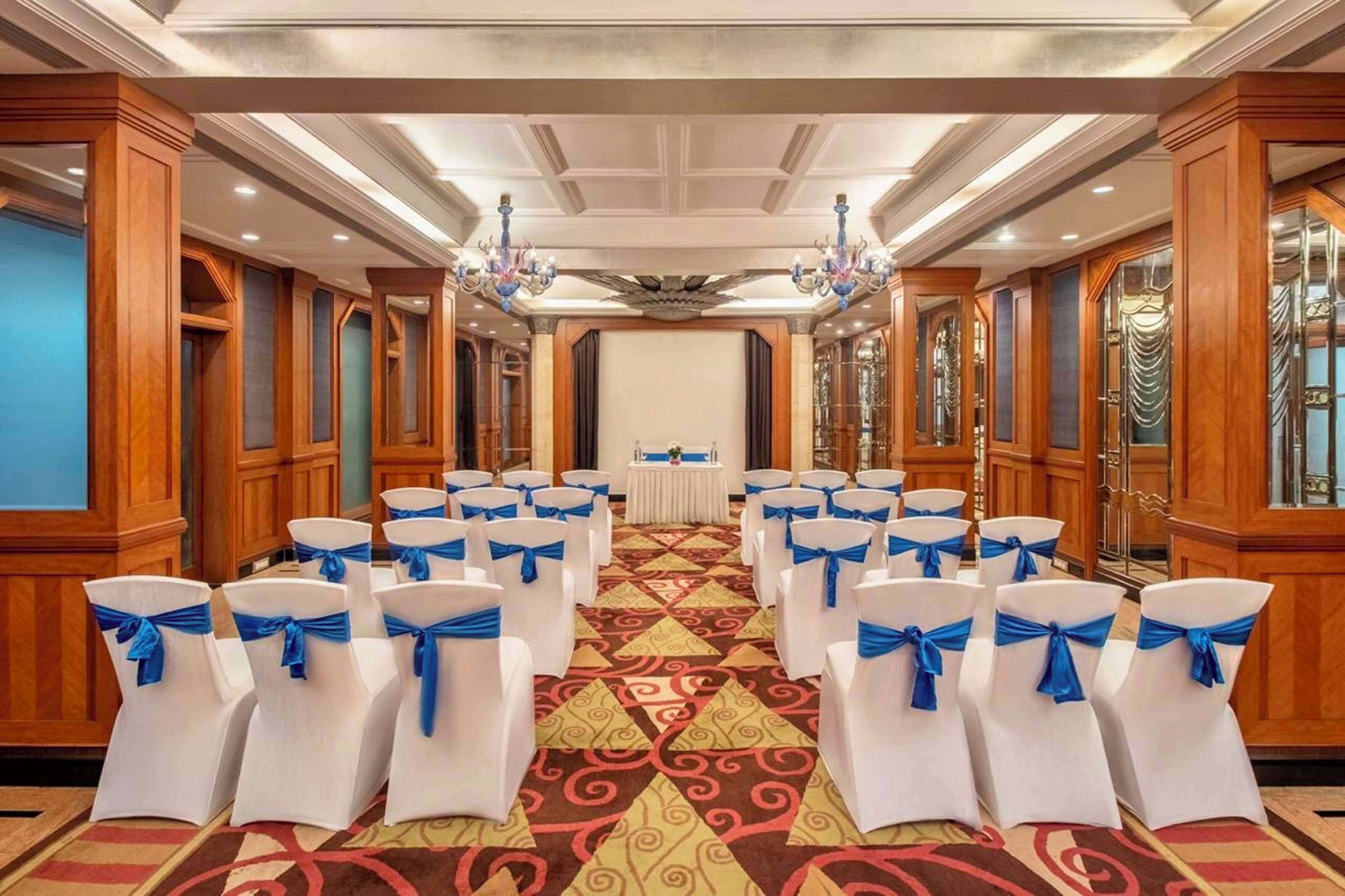 A conference room with rows of white chairs with blue sashes, a central table, and chandeliers.