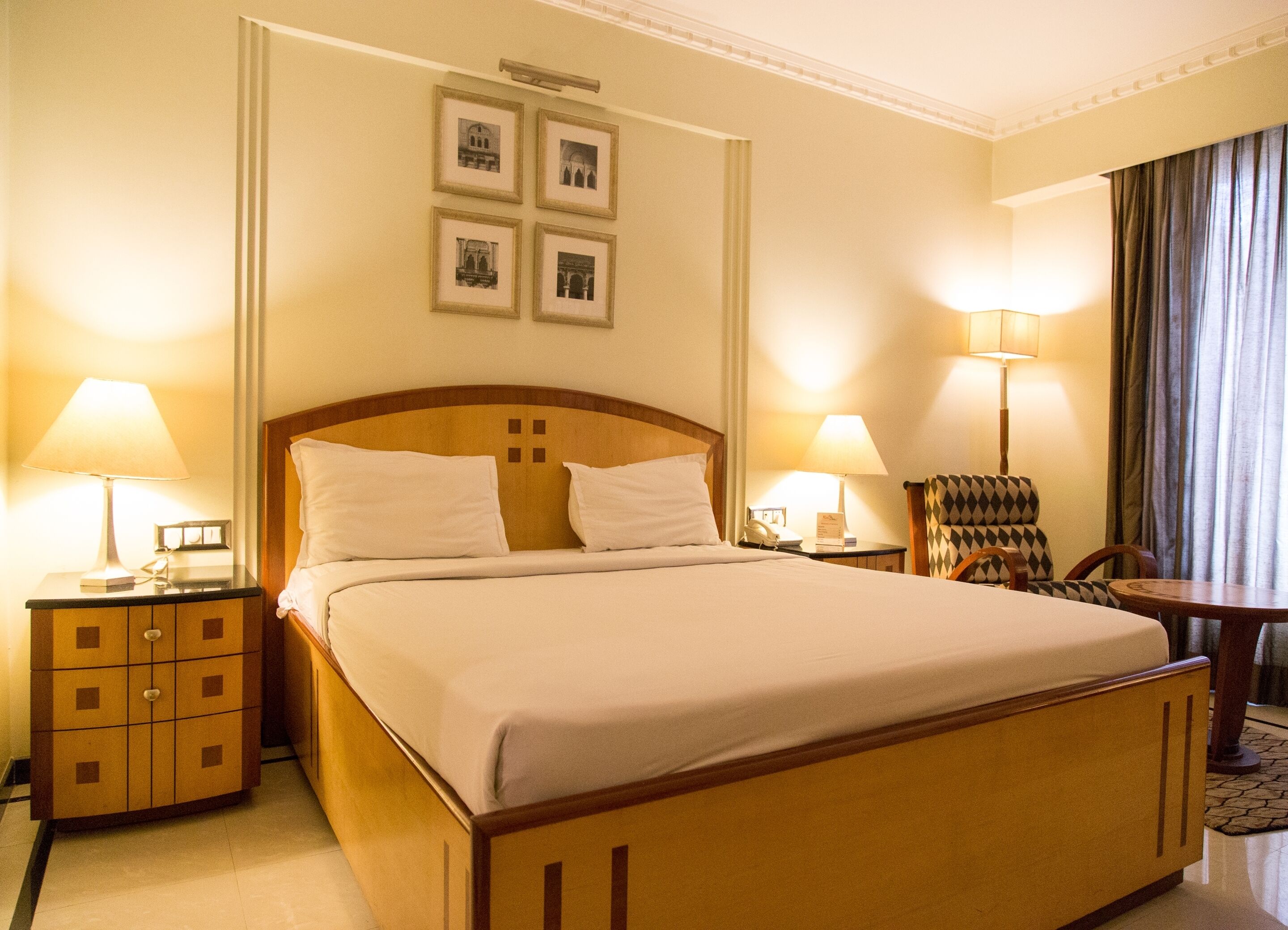 Ein Hotelzimmer mit einem großen Bett, zwei Nachttischen mit Lampen, einem Sessel und einem an der Wand befestigten Bilderrahmen.