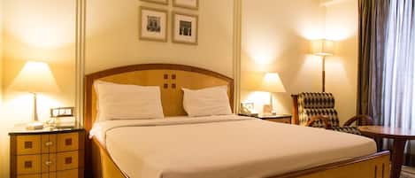 A hotel room with a large bed, two bedside tables with lamps, a chair, and a wall-mounted picture frame.