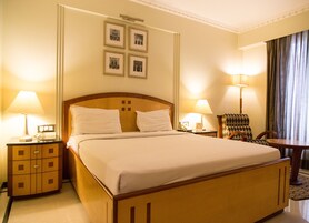 Habitación de hotel con una cama grande, dos mesitas de noche con lámparas, una silla y un cuadro colgado en la pared.