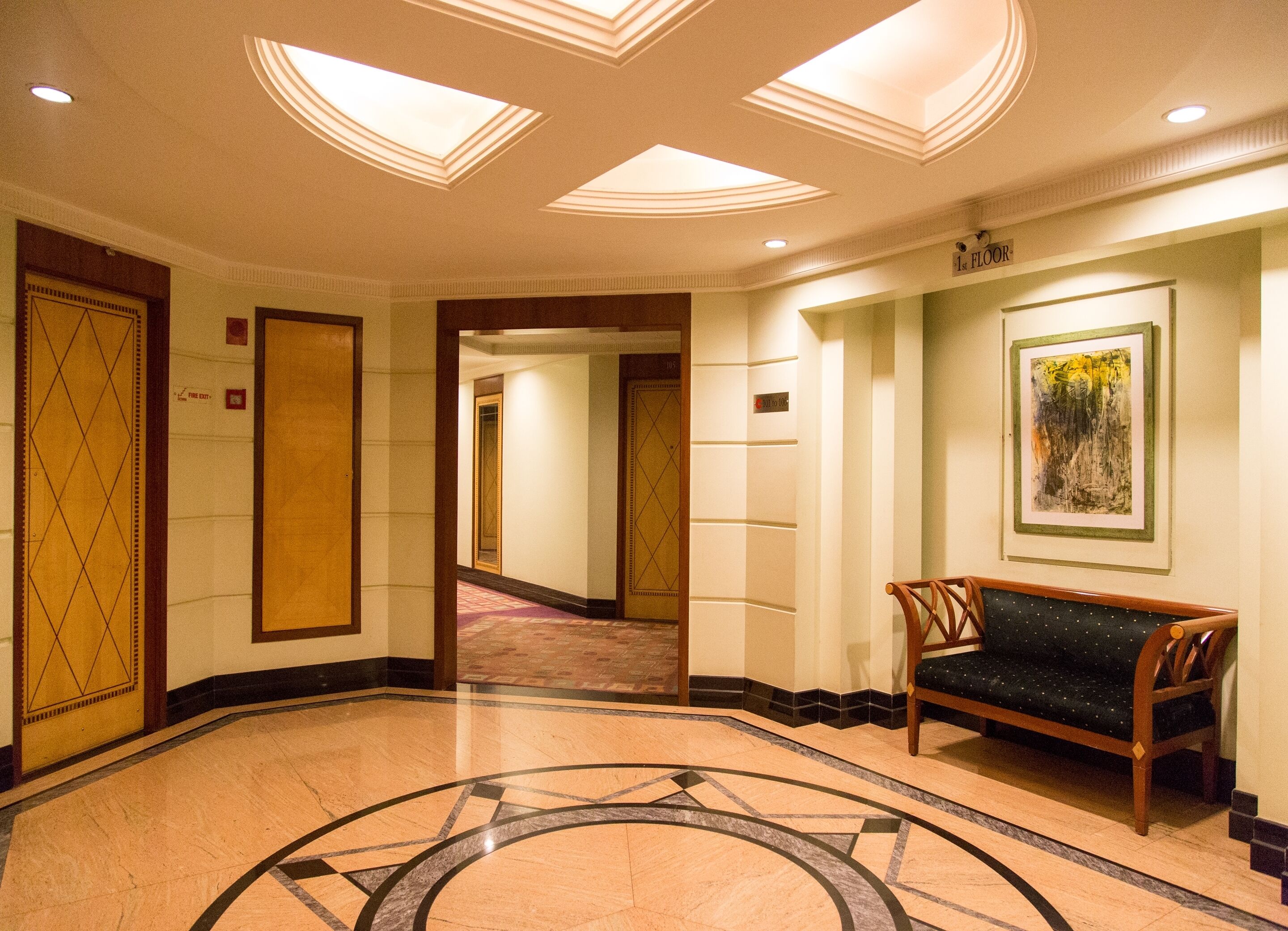 A hotel lobby with a marble floor, a bench, a framed artwork, and a door labeled "1st Floor".