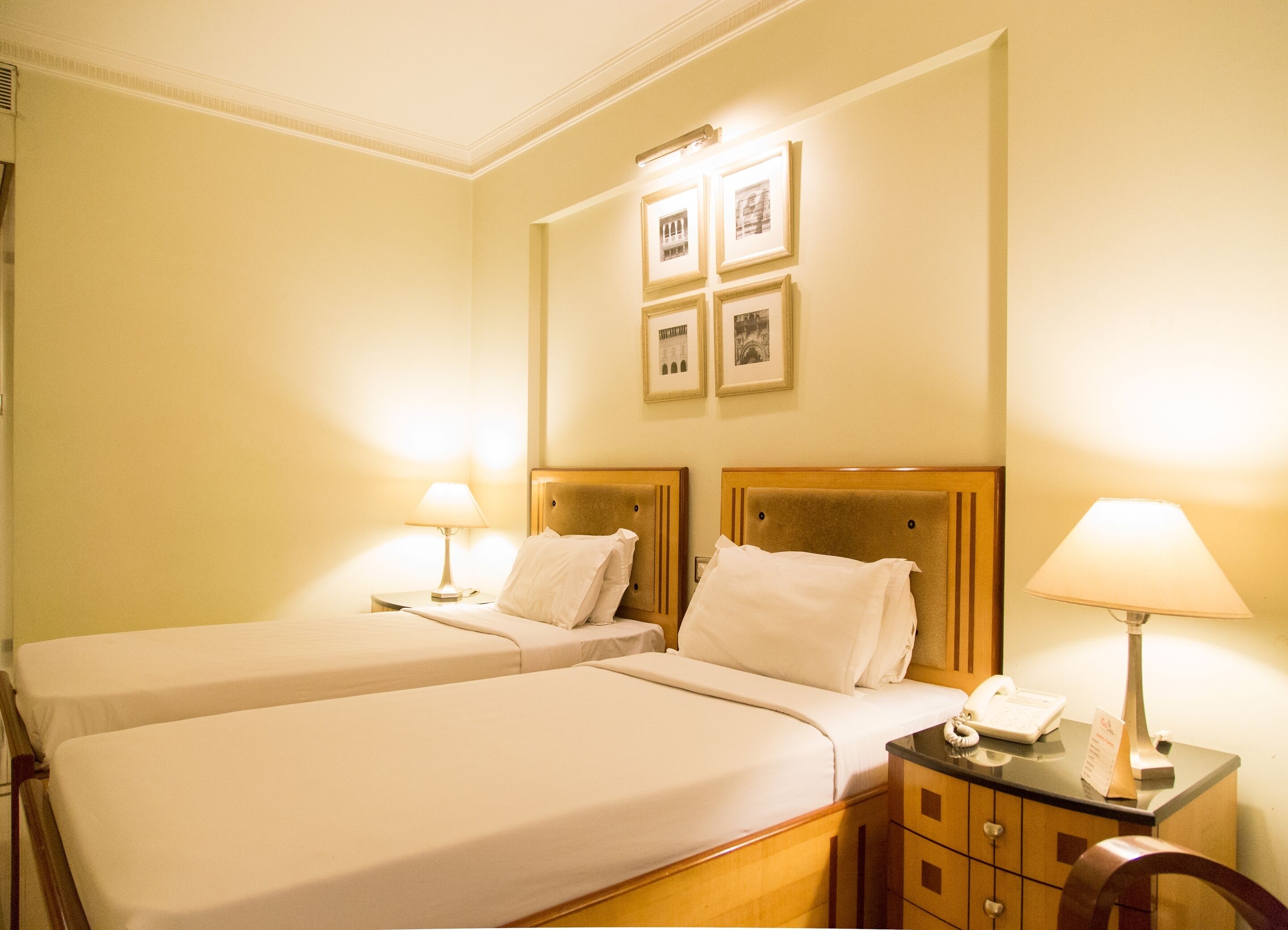 Ein Hotelzimmer mit zwei Betten, einem Holzkopfende, Nachttischen inklusive Lampen und gerahmten Bildern an der Wand.