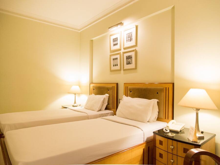 Ein Hotelzimmer mit zwei Betten, einem Holzkopfende, Nachttischen inklusive Lampen und gerahmten Bildern an der Wand.