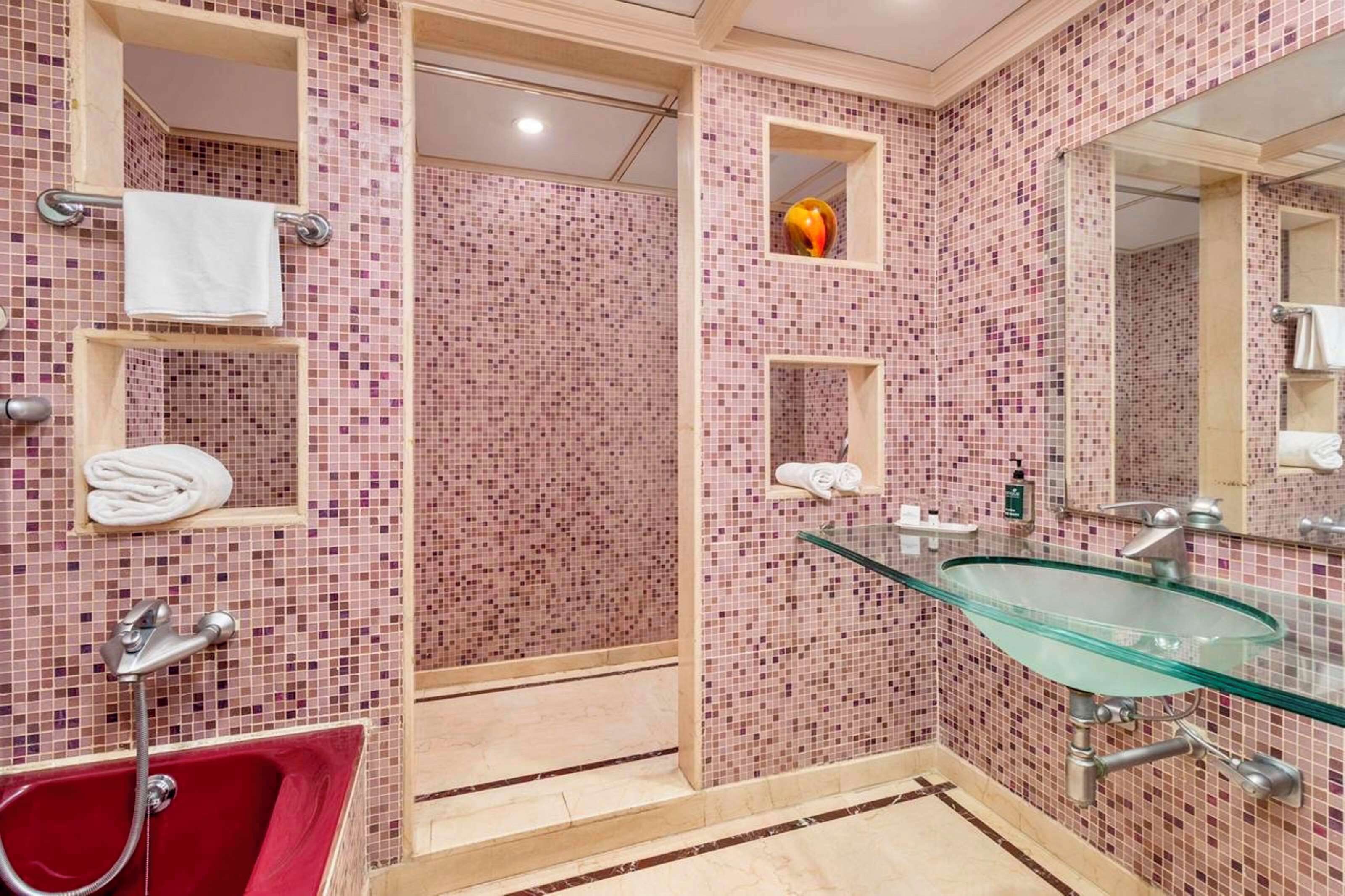 Une salle de bain avec un lavabo en verre, une baignoire rouge et des murs carrelés.