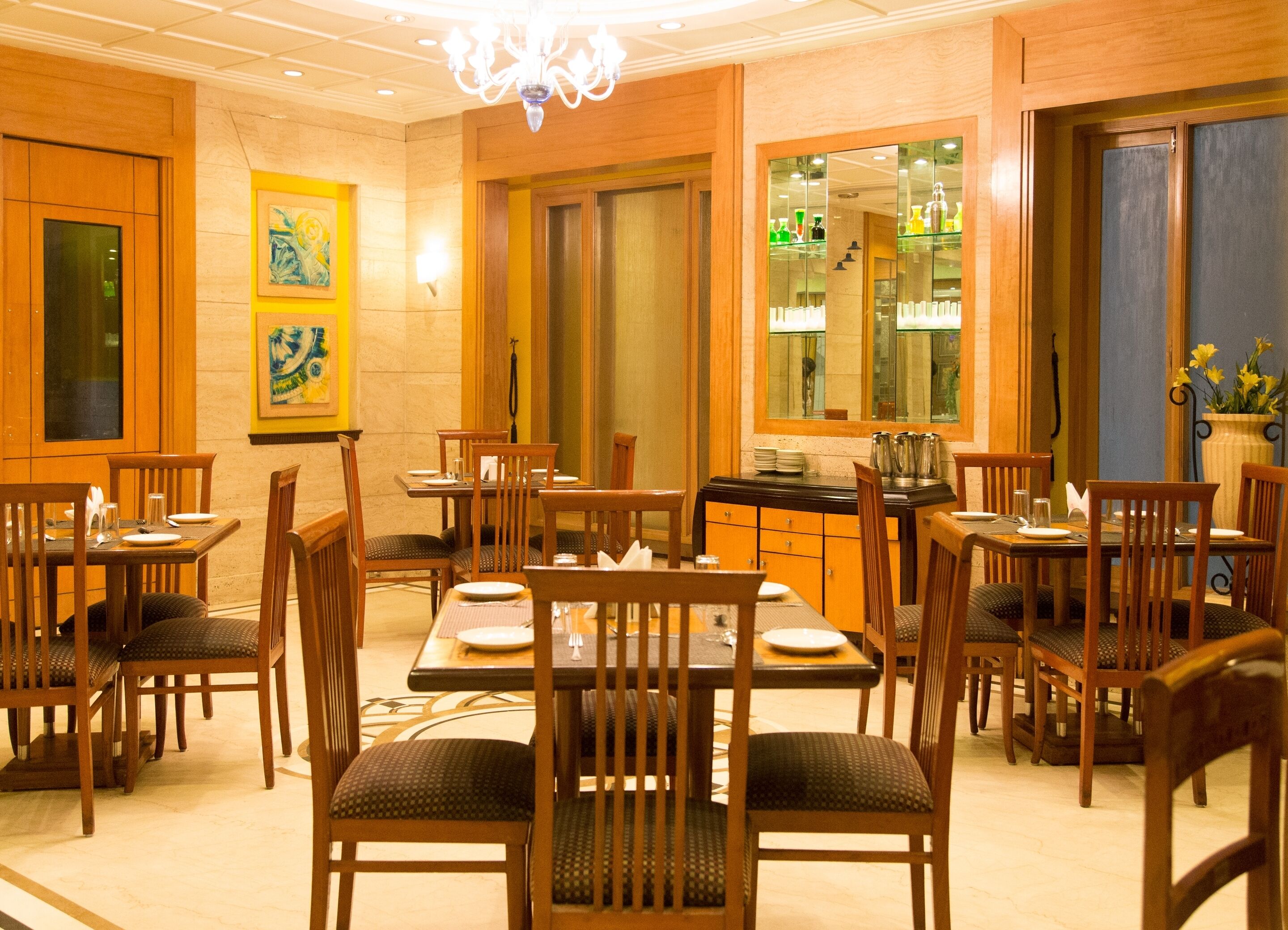A dining area with wooden tables and chairs, a chandelier, and a mirror reflecting the room.