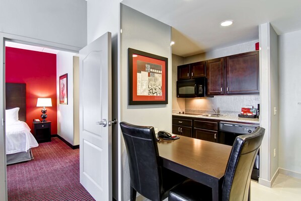 A hotel room with a dining area, a microwave, and a bed with a red accent wall.