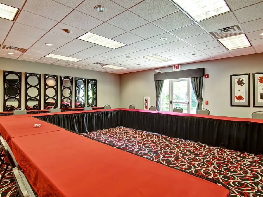 Een congreszaal met een lange tafel, stoelen en een rood tapijt.