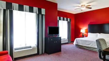 A hotel room with a bed, a desk, a television, and a ceiling fan.