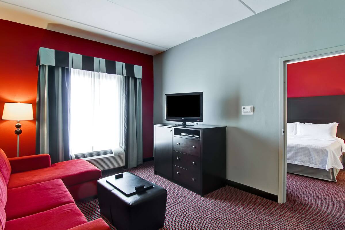 Een hotelkamer met een rode bank, een zwart tv-meubel, een bureau en een bed met witte beddengoed.